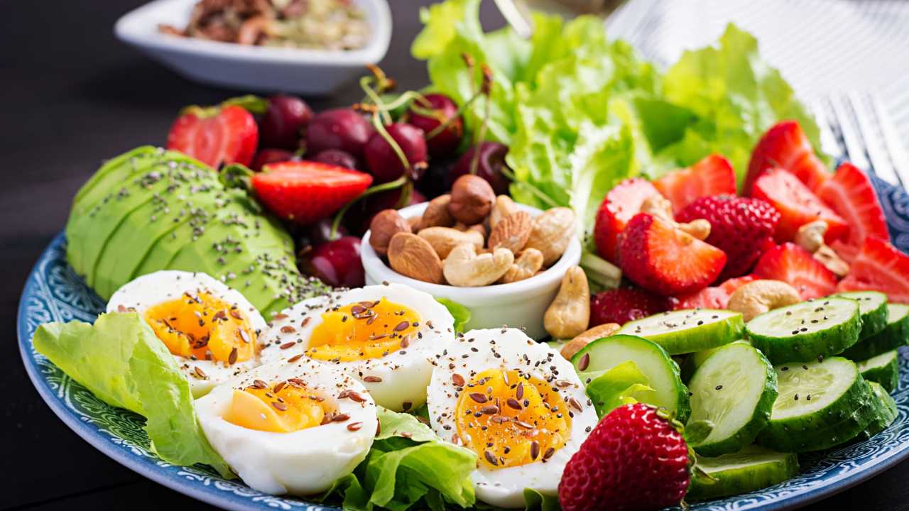 Plate filled with boiled eggs, cucumber, lettuce, avocado, nuts, and strawberries.