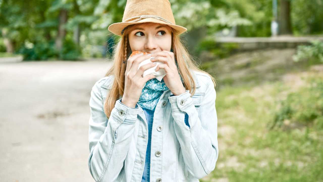 Young woman standing outside eating a hamburger.